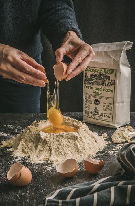 Man, cracking egg into a flour well to make pasta