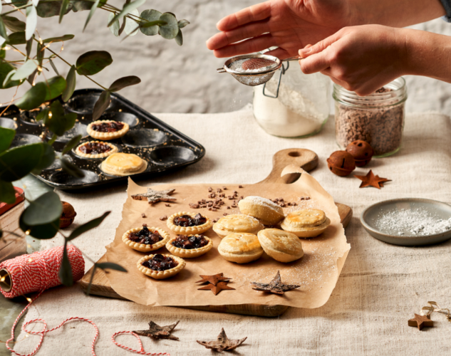 Woman sprinkling icing sugar over mince pies and mince tarts